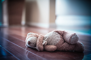 Forlorn old worn teddy bear left in empty room